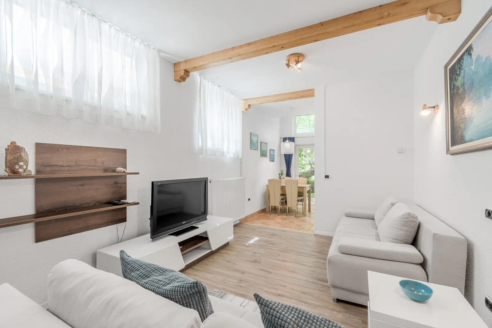 Svetel dnevni prostor apartmaja Fibula z belim kavčem in lesenimi tramovi
